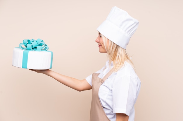 Giovane donna russa con una grande torta sopra la parete isolata con espressione felice