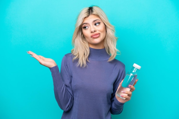 Young Russian woman with a bottle of water isolated on blue background having doubts while raising hands