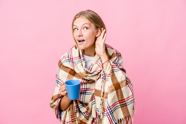 Молодая русская женщина, завернутая в одеяло, пьет кофе, пытаясь слушать сплетни.