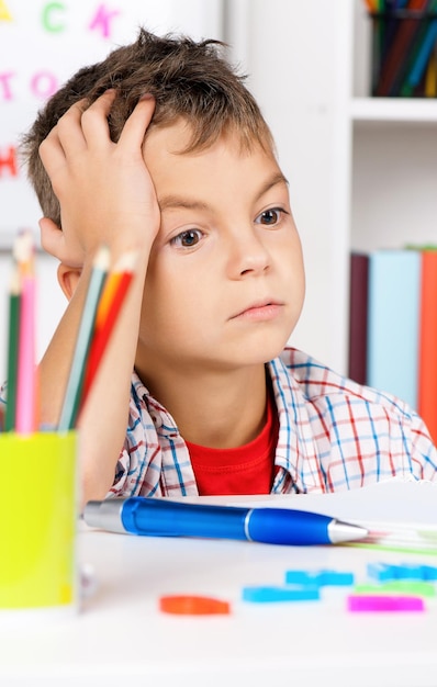 Foto giovane ragazzo triste seduto alla scrivania in classe con la testa tra le mani