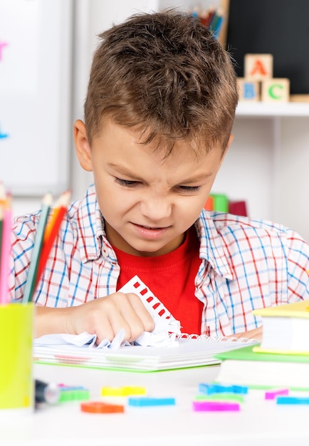 Young sad boy sitting at desk in the classroom with piece of crushed paper