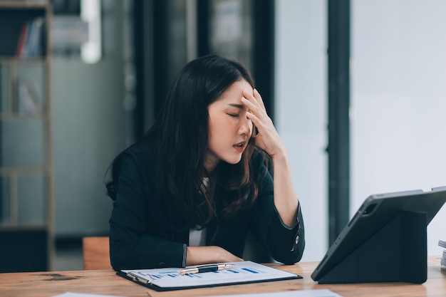Young sad businesswoman is sitting at table covering his face On desk is laptop tablet computer Stress Serious woman concentrating on his paper work