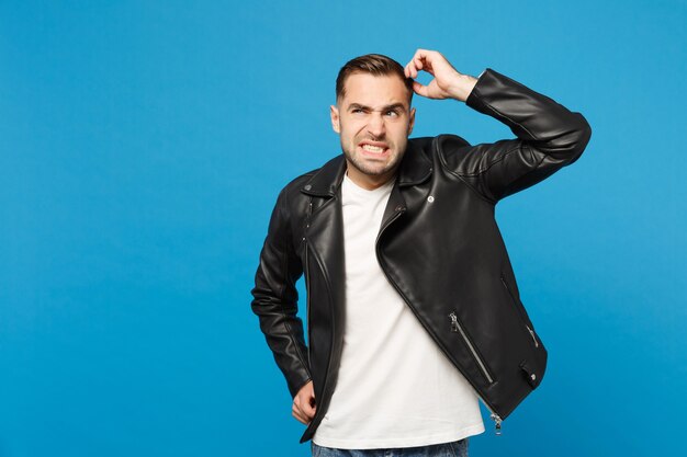 Young sad frustrated worried unshaven man in black jacket white t-shirt looking camera isolated on blue wall background studio portrait. People sincere emotions lifestyle concept. Mock up copy space.