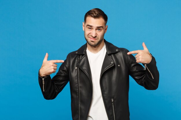 Young sad frustrated worried unshaven man in black jacket white t-shirt looking camera isolated on blue wall background studio portrait. People sincere emotions lifestyle concept. Mock up copy space.