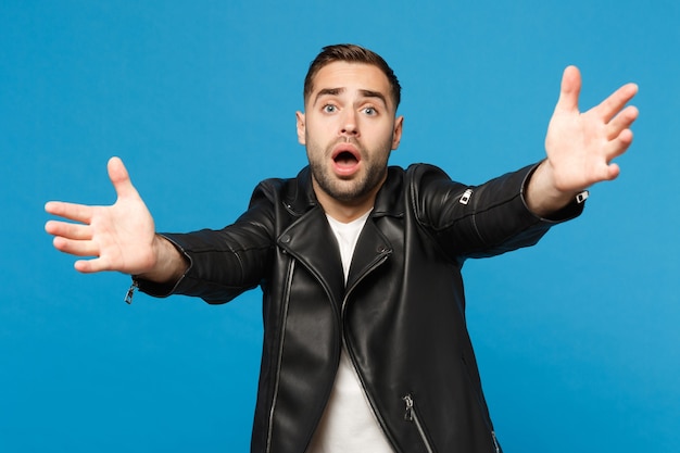 Young sad frustrated worried unshaven man in black jacket white t-shirt looking camera isolated on blue wall background studio portrait. People sincere emotions lifestyle concept. Mock up copy space.