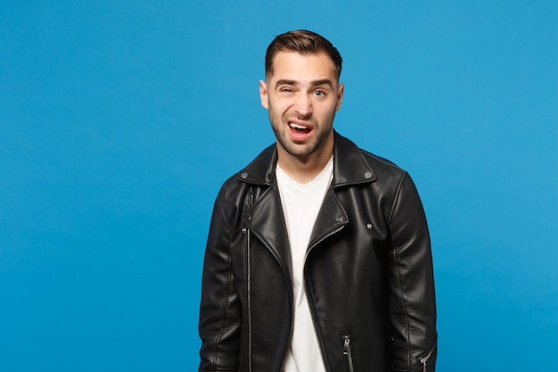 Young sad frustrated worried unshaven man in black jacket white t-shirt looking camera isolated on blue wall background studio portrait. People sincere emotions lifestyle concept. Mock up copy space.