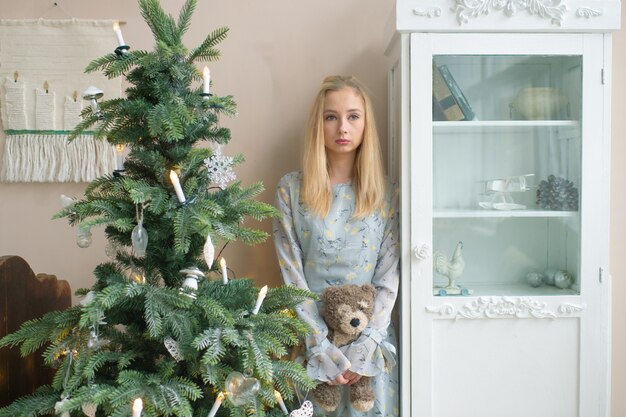 Young sad girl holding kids toy in christmas interior room with decorations