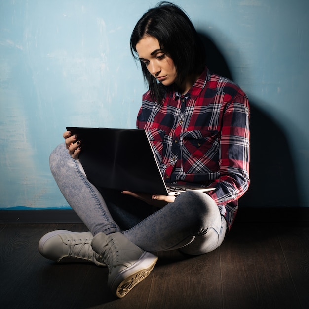 Photo young sad girl suffering from dependence on social networks sitting on the floor with a notebook