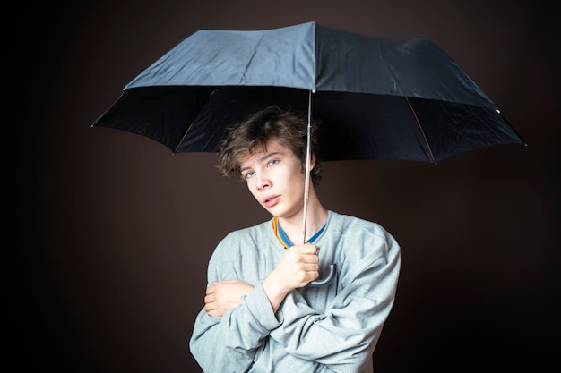 Young sad man hold umbrella in bad weather on dark background b d