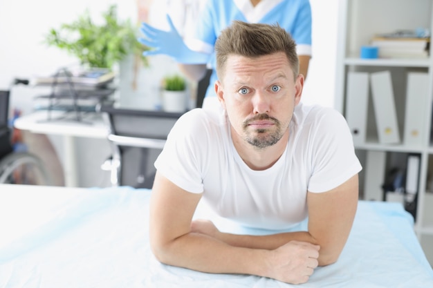 Young sad man lying on couch in front of doctor proctologist in clinic. Digital rectal examination to diagnose cancer and intestinal bleeding concept