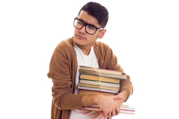 Young sad man with black hair in white Tshirt brown cardigan with glasses holding a pile of books