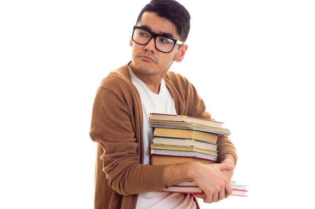 Молодой грустный мужчина с черными волосами в белой футболке и коричневом кардигане в очках держит стопку книг
