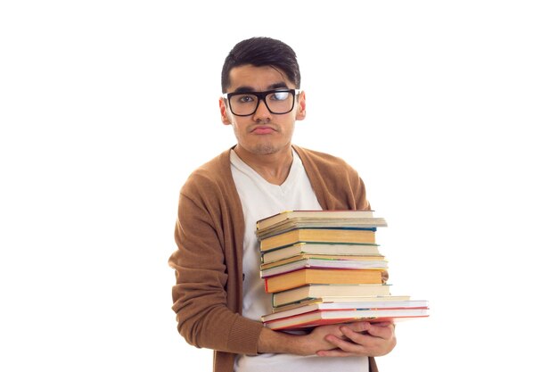 Young sad man with black hair in white Tshirt brown cardigan with glasses holding a pile of books