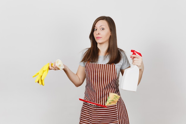 Young sad upset tired housewife in striped apron with cleaning rag squeegee in pocket isolated on white background. Woman holds smell yellow gloves spray bottle with cleaner liquid. Bottle copy space.