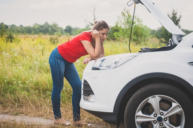 壊れた車のエンジンを見て若い悲しい女性