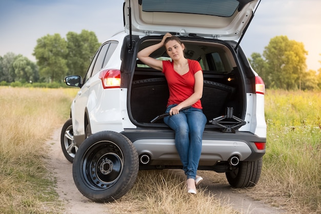 Young sad woman sitting in broken car at field