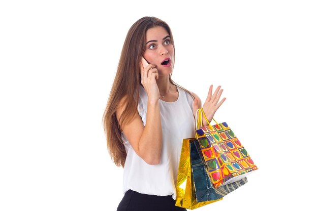 Young sad woman in white blouse and black skirt holding shopping bags and talking on the telephone