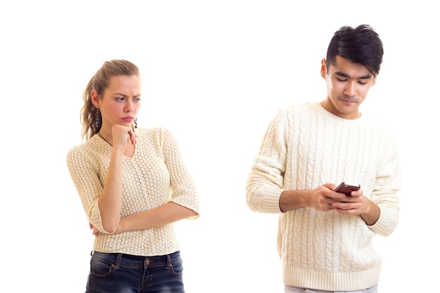 Young sad woman with long chestnut ponytail arguing with young smiling man  who is using smartphone