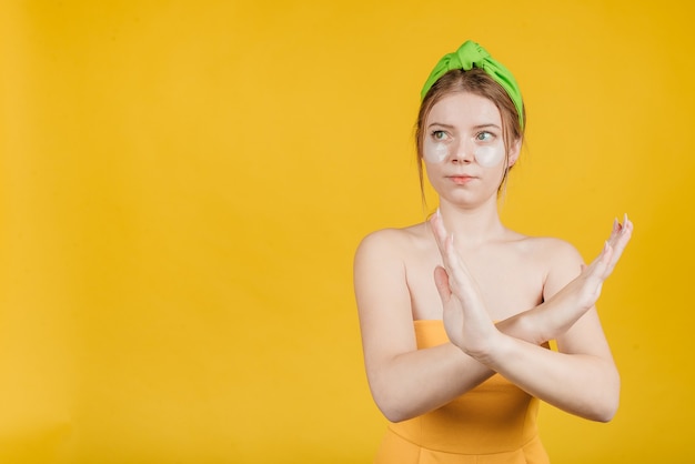 Young sad woman with patch under eyes show stop sigh eye patch no recommend isolated over yellow wall. Bad skin care routine