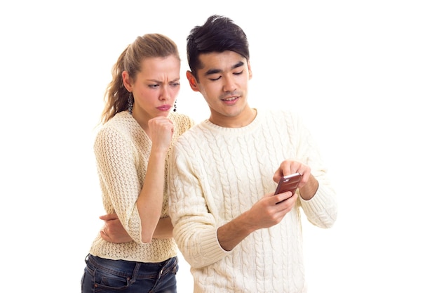 Young sad woman with young pleasant man in white sweaters and jeans using smartphone