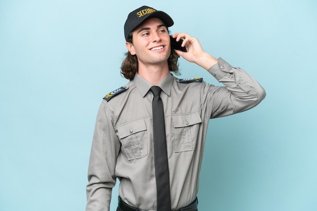 Young safeguard man isolated on blue background keeping a conversation with the mobile phone