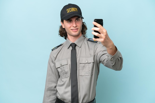 Young safeguard man isolated on blue background making a selfie