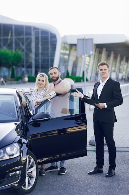 Photo a young salesman shows a new car to customers. happy young couple, man and woman buy a new car