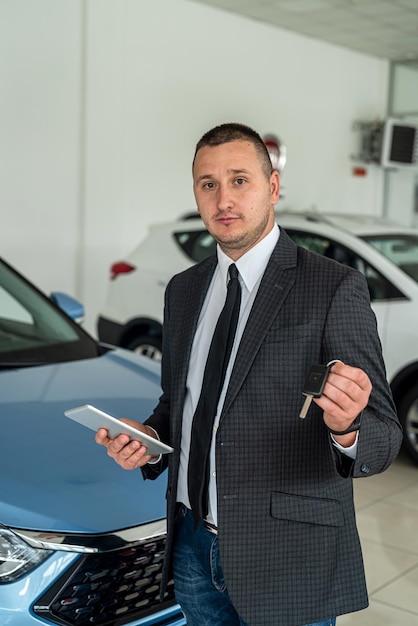 Young salesman in suit standing near at car in new modern dealership transportation concept