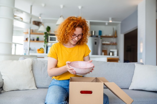 Young satisfied happy woman shopaholic customer sit on sofa unpack parcel delivery box online shopping shipment concept taking photos of product to post on social media