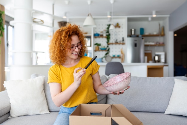 Il cliente maniaco dello shopping di giovane donna felice soddisfatto si siede sul divano disimballa il concetto di spedizione dello shopping online della scatola di consegna dei pacchi che scatta foto del prodotto da pubblicare sui social media