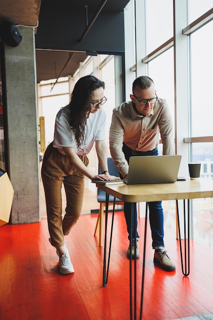 A young satisfied man talks to a female colleague and rejoices in the work done Colleagues work at a laptop in the office Work in a modern office space