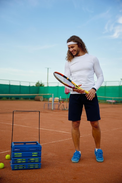 Молодой довольный теннисист собирает разбросанные мячи по полю после игры