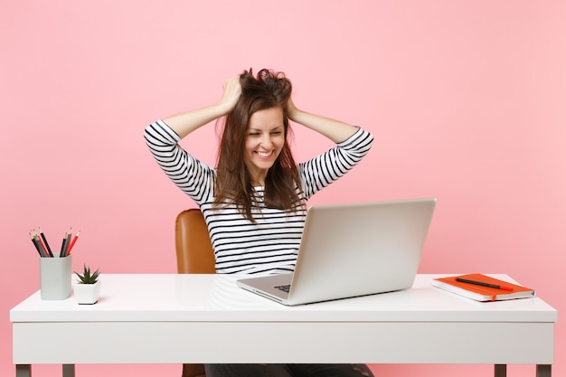 Young satisfied woman clinging to hair, head finish working complete project with pc laptop while sitting at office 