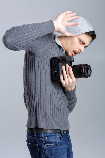 사진 dslr 디지털 카메라 사진가와 함께 셔츠를 입은 젊은 겁 먹은 사진 작가는 회색 배경에 손으로 닫습니다