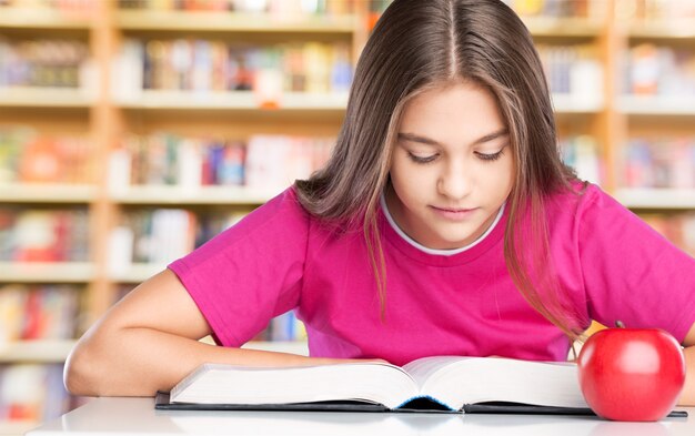 Young school girl reading a book at the library