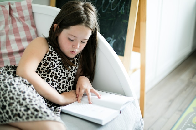 Young school girl reading a book in the room at home.