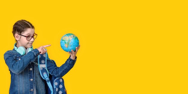 Young school teen kid girl 8-9 years old with backpack hold in hand globe world isolated on yellow background children studio portrait education travel abroad lifestyle concept. long wide banner