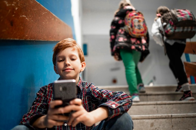 Young schoolboy using his smart phone in school and browsing internet or checking social networks.