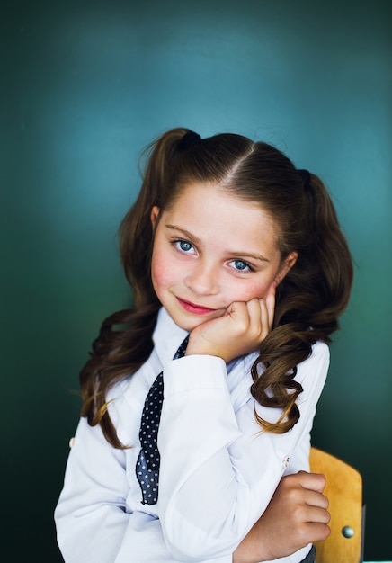 Young schoolgirl near the blackboard in a white shirt and tie