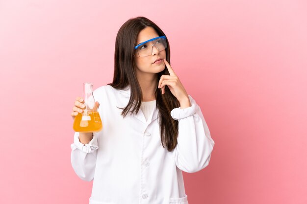 Young scientific girl over isolated pink background having doubts while looking up