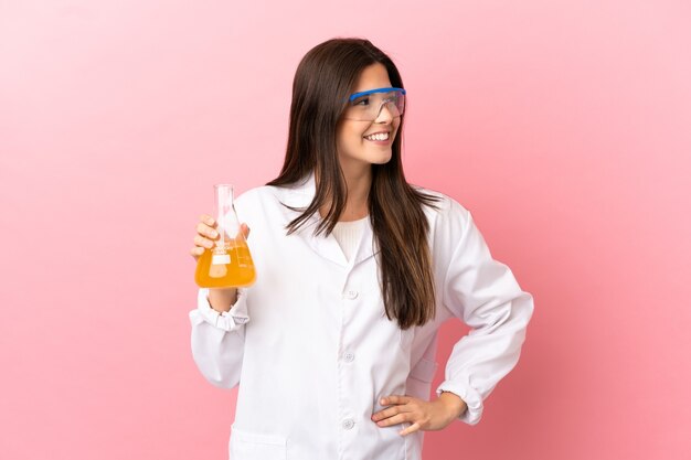 Giovane ragazza scientifica su sfondo rosa isolato in posa con le braccia all'anca e sorridente