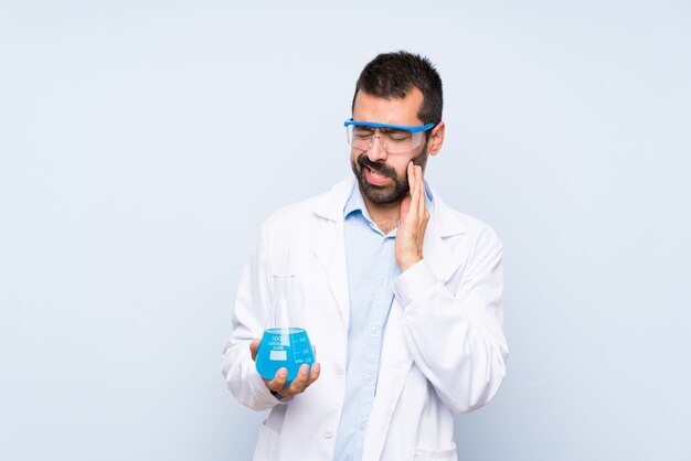 Young scientific holding laboratory flask over isolated background with toothache