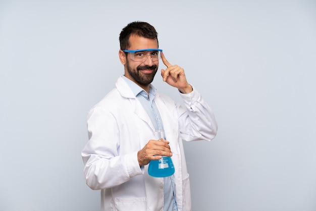 Young scientific holding laboratory flask over isolated wall with glasses and smiling