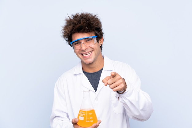 Young scientific man over isolated blue wall points finger at you