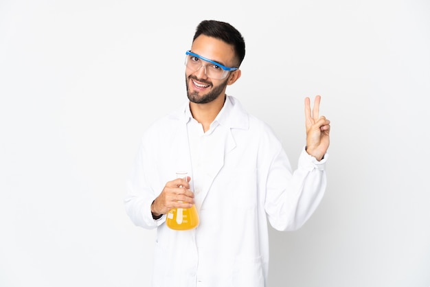 Young scientific man isolated on white wall smiling and showing victory sign