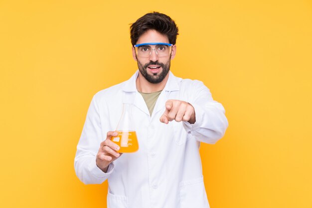 Young scientific man over isolated yellow wall surprised and pointing front