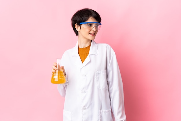 Young scientific woman isolated on pink wall looking side