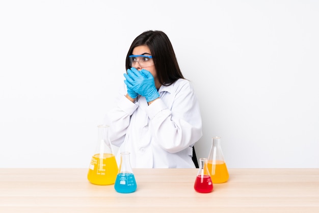 Young scientific woman in a table covering mouth and looking to the side