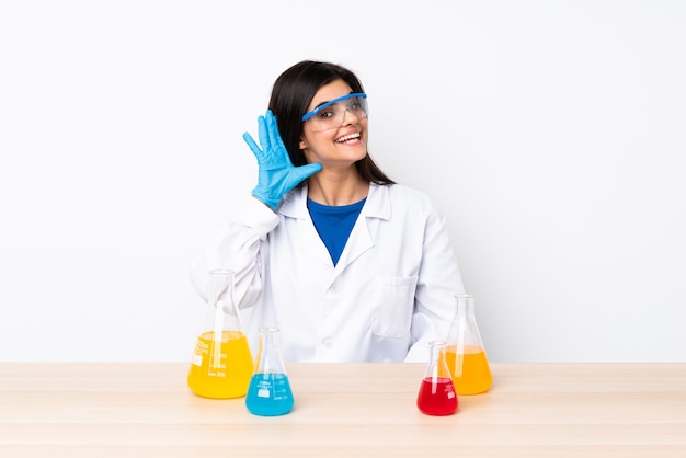 Young scientific woman in a table listening to something by putting hand on the ear