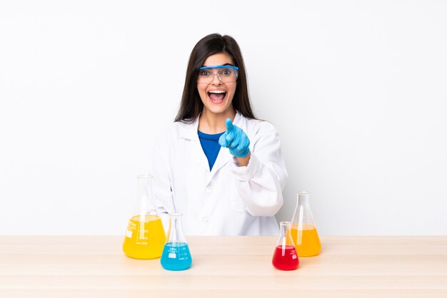 Young scientific woman in a table surprised and pointing front